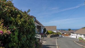 A residential street with houses, a clear sky, and a view of the sea.