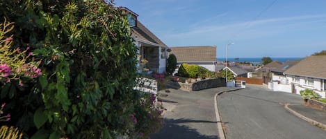 A residential street with houses, a clear sky, and a view of the sea.