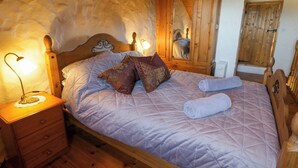 A wooden bed with a headboard, a bedside table with a lamp, and a mirror on the wall.