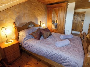 A wooden bed with a headboard, a bedside table with a lamp, and a mirror on the wall.