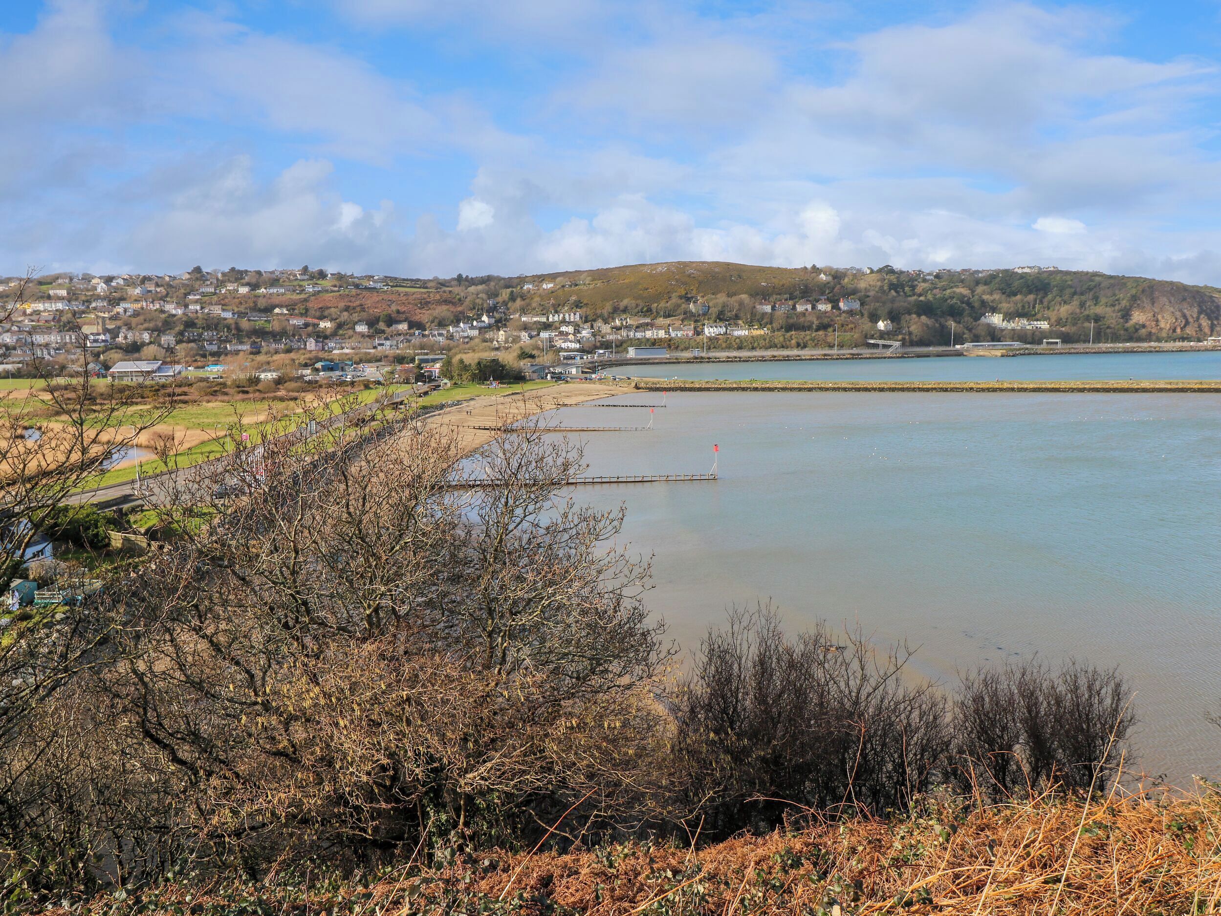A coastal town with a calm bay, houses along the shore, and a hill in the background.