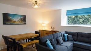 Una sala moderna con una mesa de comedor de madera, un sofá gris con cojines azules, un banco de madera, una lámpara y un cuadro en la pared.