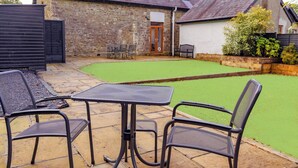 Un patio con una mesa y sillas, un muro de piedra y un césped.