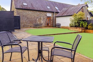 A patio with a table and chairs, a stone wall, and a grassy lawn.