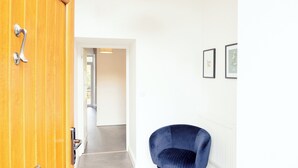 Un pasillo con una puerta de madera, una silla azul y cuadros en la pared.