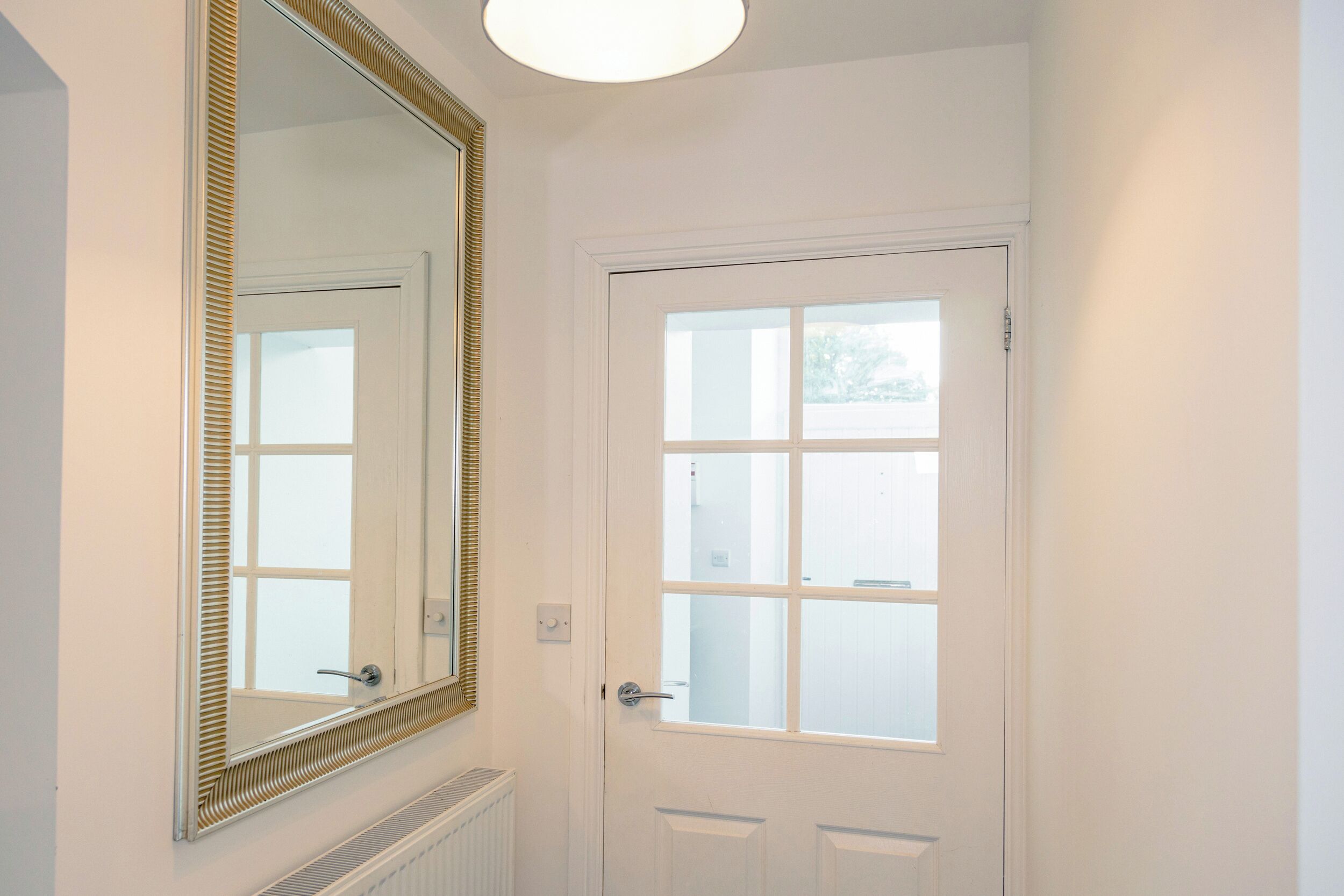 A bathroom with a white door, a large mirror with a gold frame, and a window above the door.
