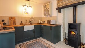 A modern kitchen with dark cabinetry, a built-in microwave, and a stone fireplace. - Gingerbread House (Thurso)