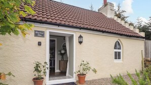 A cottage with a tiled roof, a door leading to a room, and potted plants around the entrance. - Gingerbread House (Thurso)