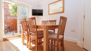 A dining area with a wooden table and chairs, a TV mounted on the wall, and a sliding glass door leading to an outdoor patio. - 6 Willows Green (Aldeburgh)