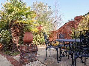 Un patio con pared de ladrillo, una planta grande en maceta y mobiliario de exterior de metal.