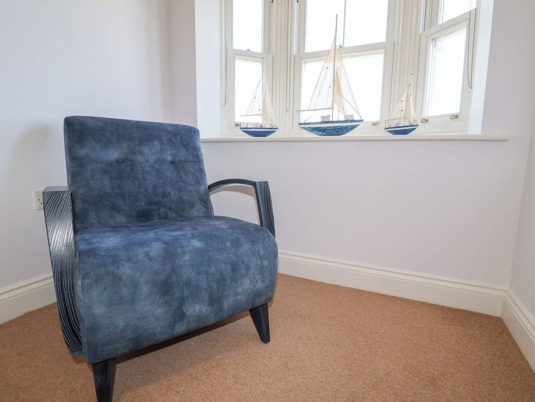 A blue armchair in a room with a beige carpet and a window with three sailboats.