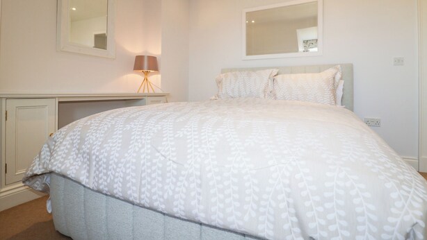 A bedroom with a large bed, a bedside table, a lamp, and a mirror on the wall. - 6 Willows Green (Aldeburgh)