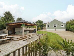 A wooden deck with outdoor furniture, a covered seating area, and a house with a green exterior. - Woodside Guest House (Coleraine)