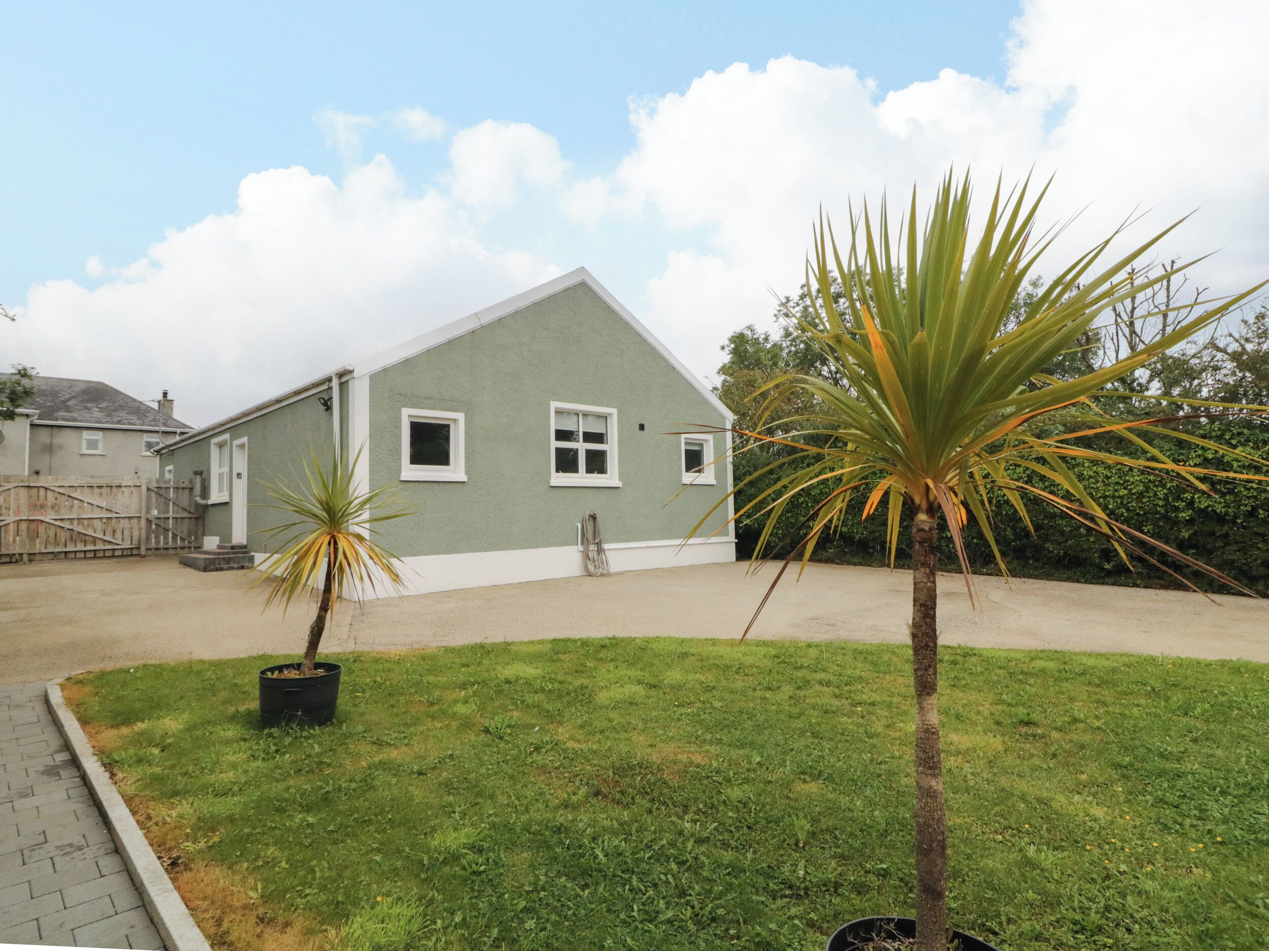 A single-story building with a flat roof, a small front yard with grass and two potted plants, and a clear sky with clouds.