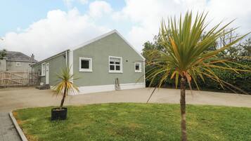A single-story building with a flat roof, a small front yard with grass and two potted plants, and a clear sky with clouds.