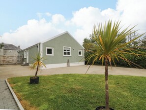 A single-story building with a flat roof, a small front yard with grass and two potted plants, and a clear sky with clouds. - Woodside Guest House (Coleraine)