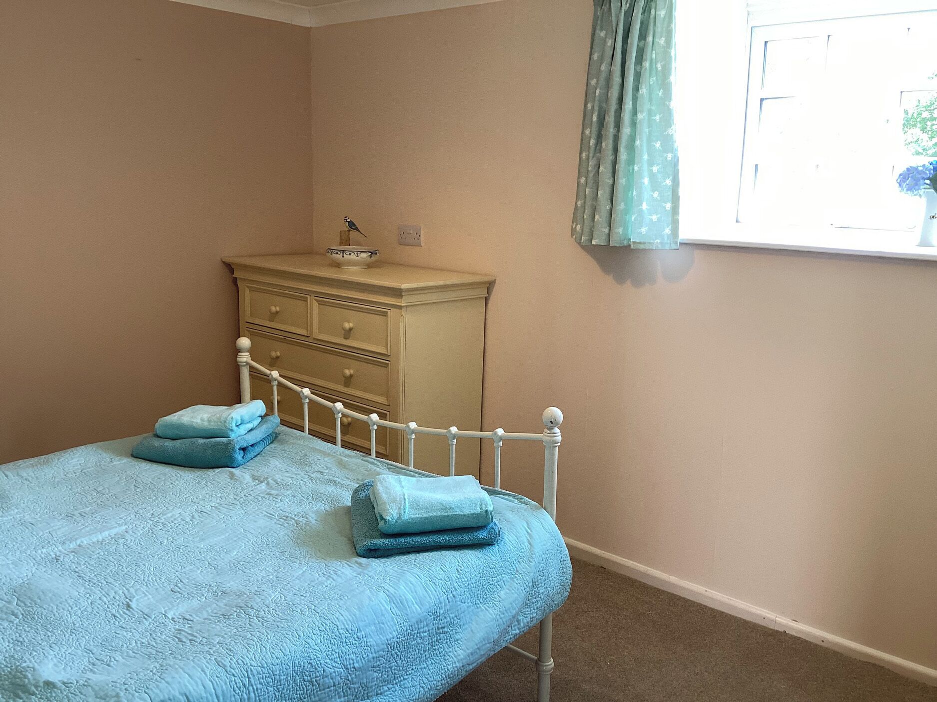 A bedroom with a bed, a dresser, and a window with curtains.