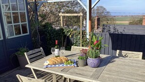 Mesa de madeira ao ar livre com pão, uma garrafa de vinho e plantas em vasos.