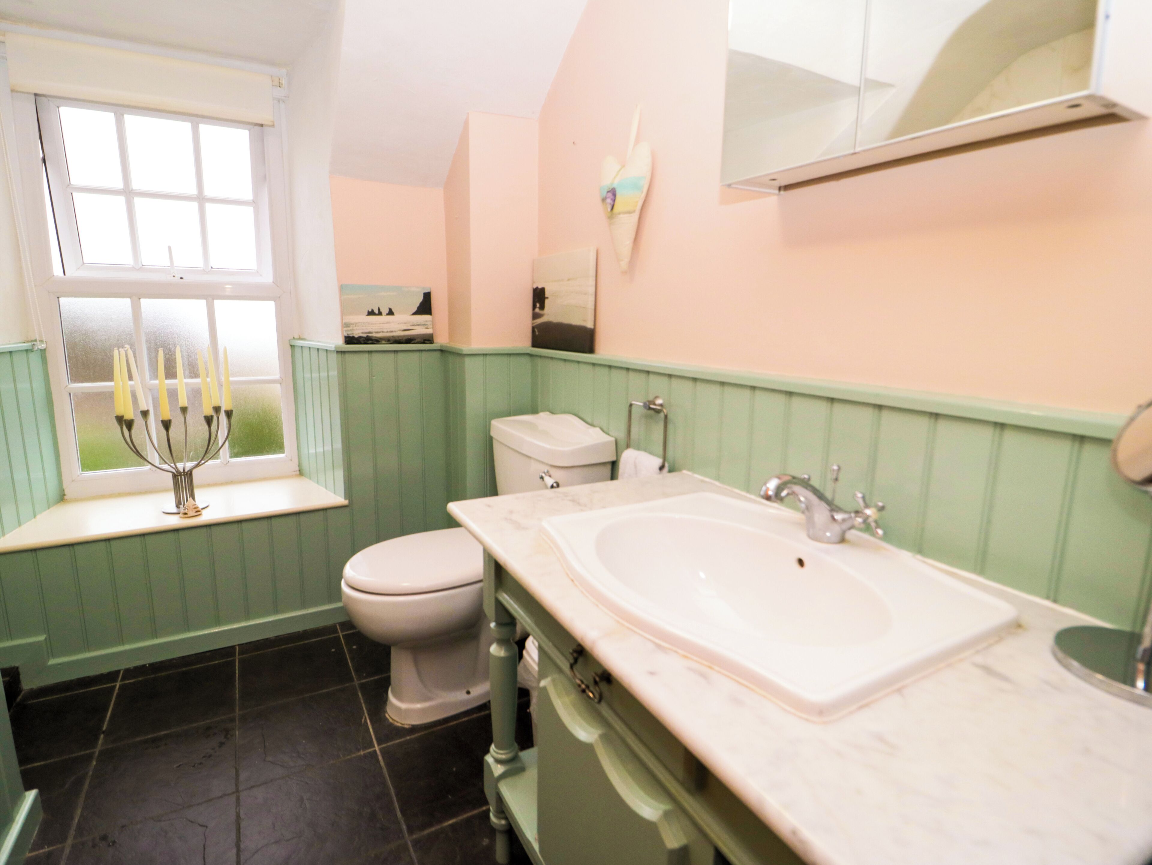 A bathroom with a white sink, a toilet, and a window with a candle holder.