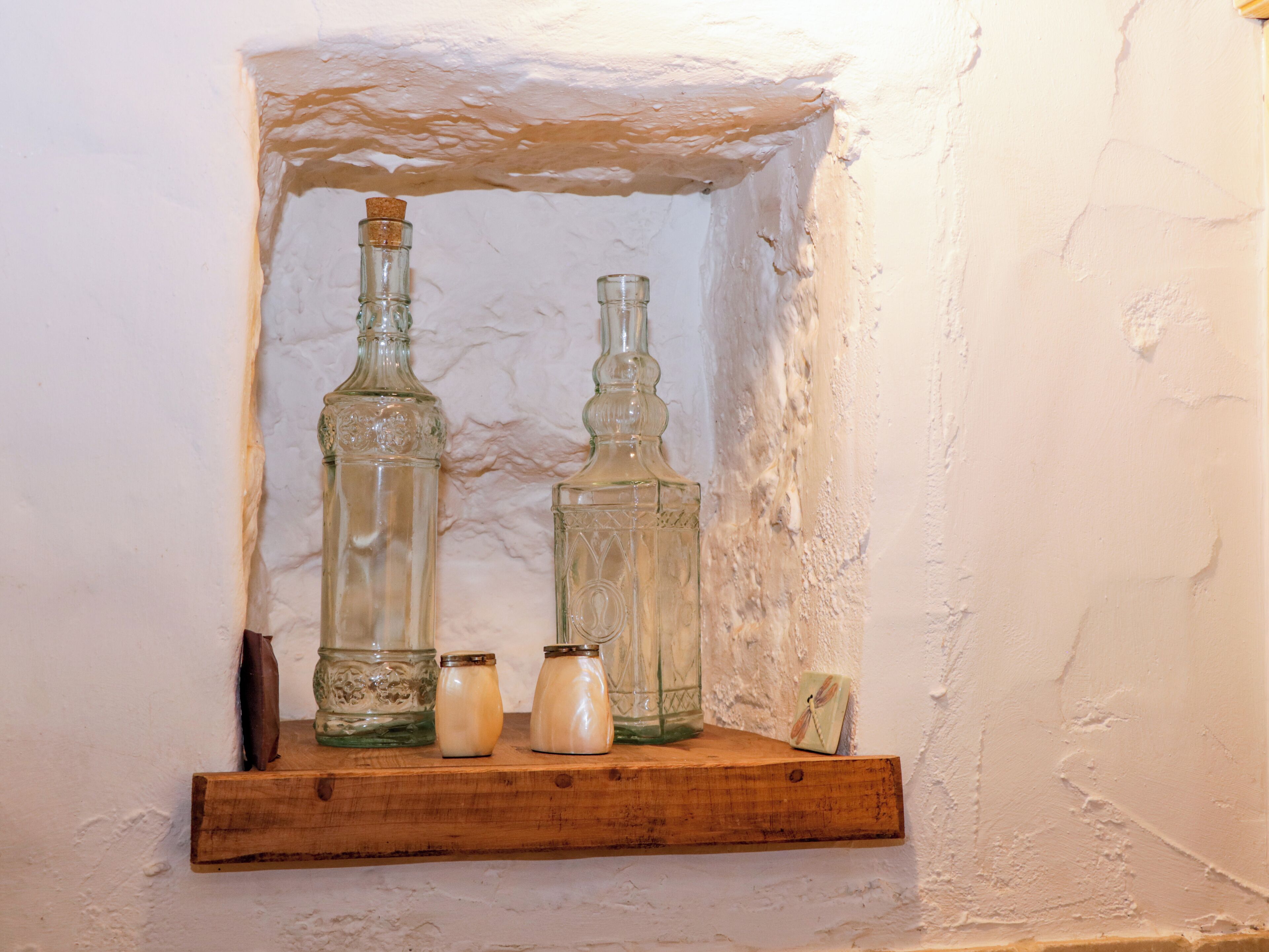 Ein Holzregal mit zwei Glasflaschen und zwei kleinen Gläsern vor einer strukturierten Wand.