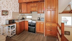 A kitchen with wooden cabinets, a microwave, a toaster, and a kettle. - 11 South Snowdon Wharf (Porthmadog)