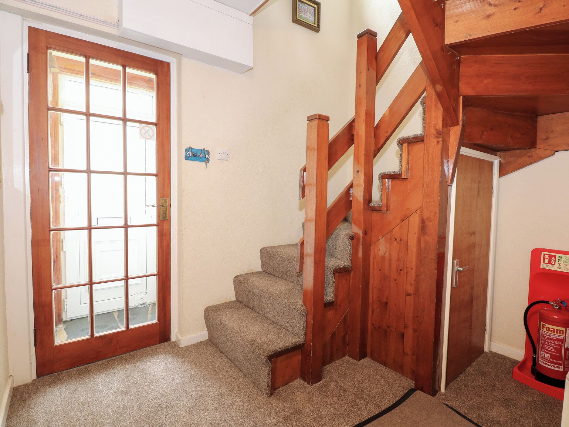 A staircase with wooden railings leading to an upper floor, carpeted steps, and a fire extinguisher on the right.