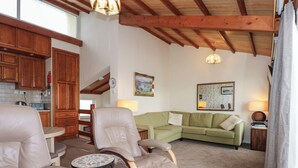 A cozy living room with a green sofa, two leather chairs, a small table, and a kitchen in the background. - 11 South Snowdon Wharf (Porthmadog)