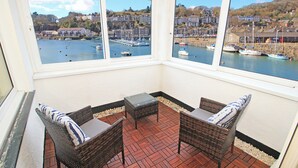 En overdækket terrasse med fletningsmøbler og udsigt til en havn.