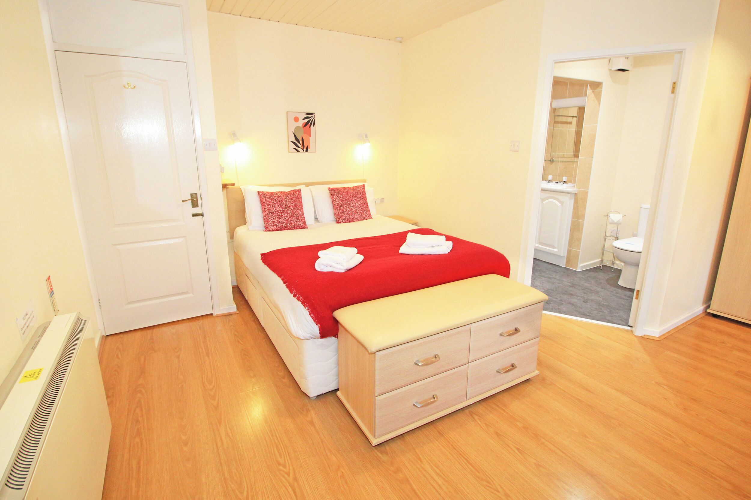 A hotel room with a bed, bedside tables, a bathroom visible through an open door, and a radiator.