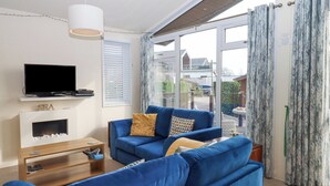 A modern living room with a blue sofa, a flat-screen TV, a fireplace, and large windows with curtains. - Matilda Lodge (Plymouth)