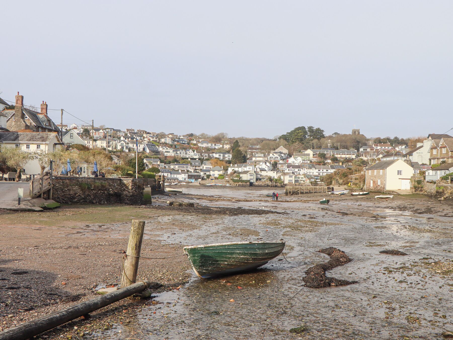 Une ville côtière avec un bateau vert sur la plage, des murs de pierre et des maisons en arrière-plan.