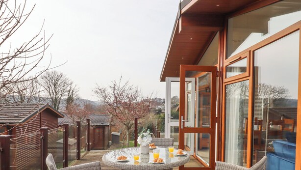 A deck with wicker chairs and a glass table set for breakfast. - Matilda Lodge (Plymouth)