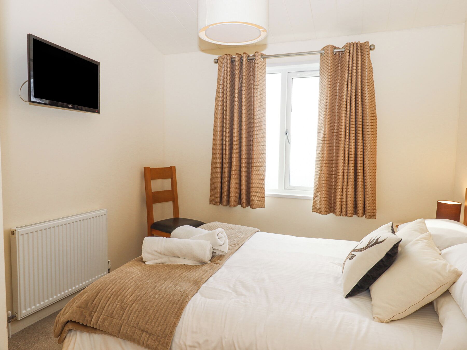 A hotel room with a bed, a chair, a television mounted on the wall, and a window with curtains.