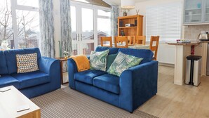 A living room with a blue sofa, a patterned rug, and a dining area with a wooden table and chairs. - Matilda Lodge (Plymouth)