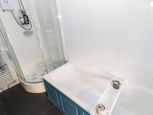A modern bathroom with a glass-enclosed shower, a bathtub with a built-in seat, and a white tiled wall.