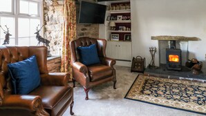 A cozy living room with leather armchairs, a fireplace, a stone wall, and a television. - Rose Hip Cottage (Hexham)