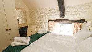 A bedroom with a stone wall, a wooden bed frame, a green bedspread, and a white bedspread. - Rose Hip Cottage (Hexham)