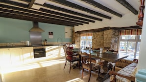 A spacious kitchen with a stone wall, wooden beams, and a large dining table set for four. - Rose Hip Cottage (Hexham)