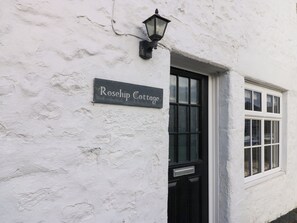 A white cottage with a black door and a sign reading "Rosehip Cottage".
