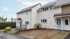 A two-story residential building with a white exterior, a front door with a number plaque, and a small front garden with gravel and a potted plant. - Green Cottage (Porthmadog)