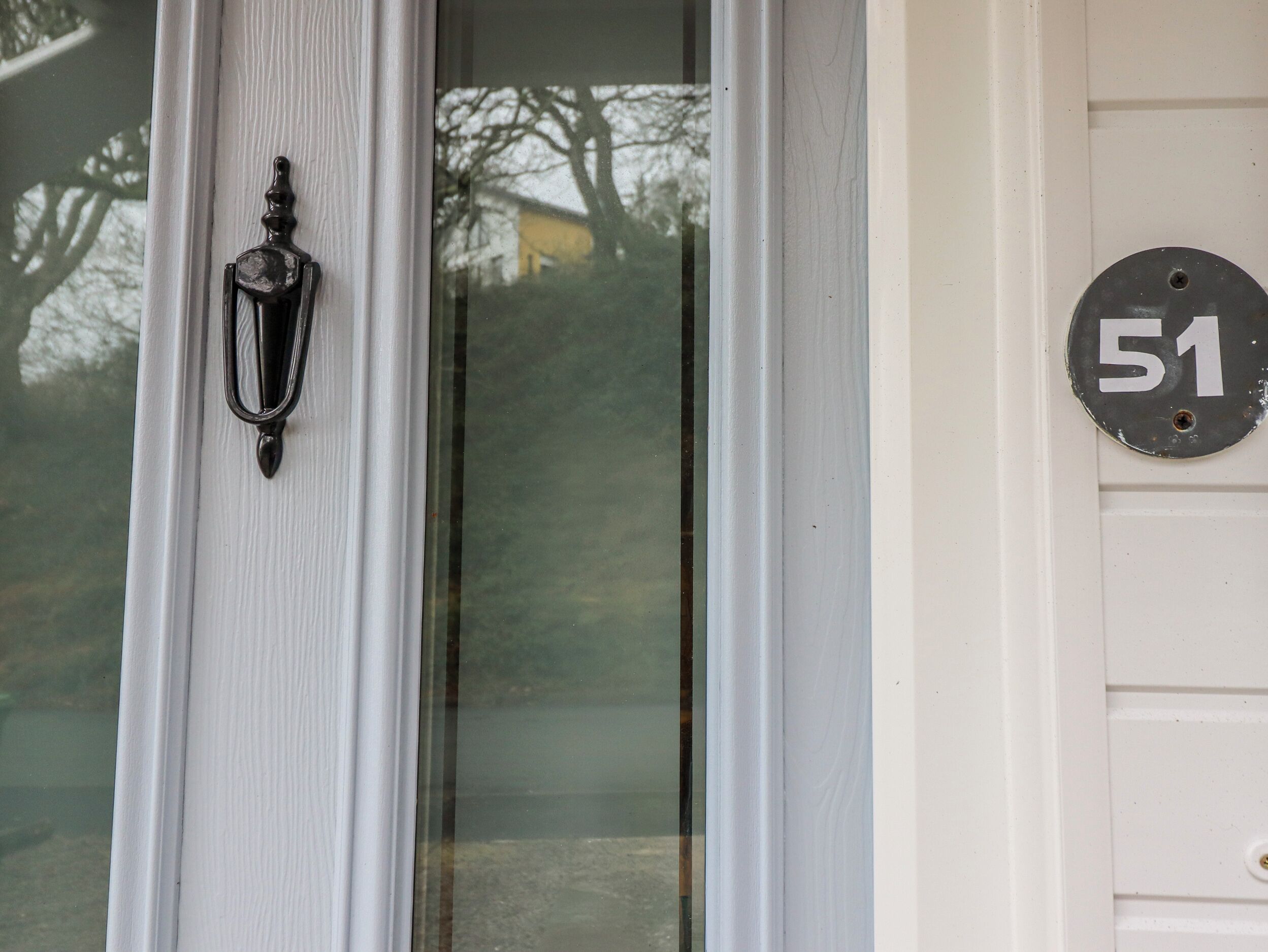 A white door with a black doorbell and a house number plaque.