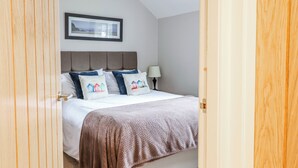 A bedroom with a bed, a headboard, a bedside table, a lamp, and a framed picture on the wall. - Green Cottage (Porthmadog)