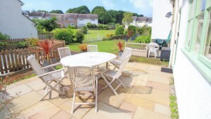 An outdoor patio with a round table and four chairs, a wooden fence, and a view of houses in the background. - Green Cottage (Porthmadog)