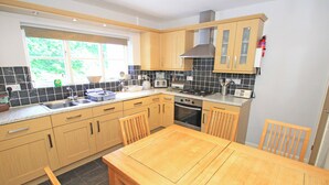 A modern kitchen with wooden cabinets, a large island, and a gas stove. - Green Cottage (Porthmadog)