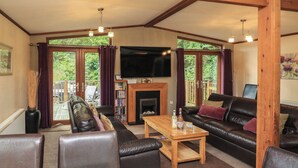 A spacious living room with a fireplace, leather sofas, a coffee table, and a television. - Templar Rise 16 - Devon Comfort (Newton Abbot)