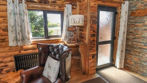 A log cabin interior with a leather armchair, a fireplace, and a view of the outdoors. - Stag Lodge Holiday Retreat (Whitby)