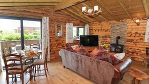 A log cabin interior with a wooden dining table, chairs, a sofa, a television, and a fireplace. - Stag Lodge Holiday Retreat (Whitby)