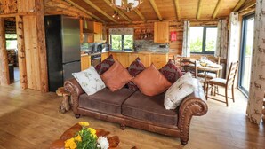 A cozy cabin interior with a wooden dining table, a brown leather sofa with patterned cushions, and a kitchen area with wooden cabinets and a black refrigerator. - Stag Lodge Holiday Retreat (Whitby)