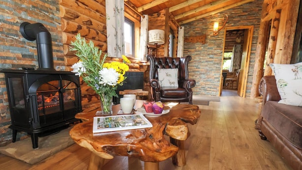 A cozy cabin interior with a wooden table, a fireplace, a leather armchair, and a sofa. - Stag Lodge Holiday Retreat (Whitby)