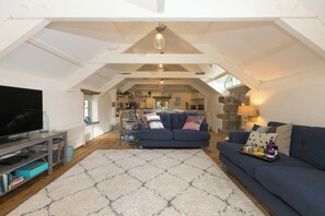 Ein geräumiges Loft mit hoher Decke, einem großen Fernseher, einer Couch und einem Essbereich.